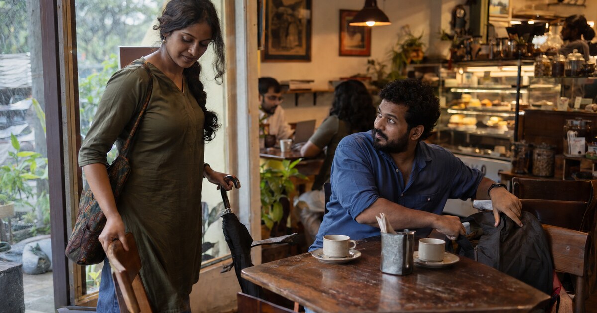 At a small neighbourhood café in Kochi in the late afternoon, a South Asian woman around 30 with brown skin and dark hair in a loose braid,…